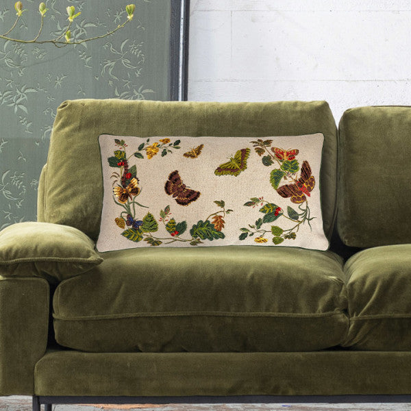 A rectangular cotton lumbar pillow with an embroidered butterfly and flower design on a beige mud cloth background, featuring green piping around the edges.